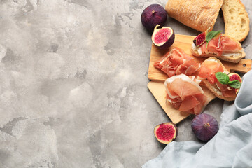 Wooden board of bread slices with delicious prosciutto and fresh fig on grey background