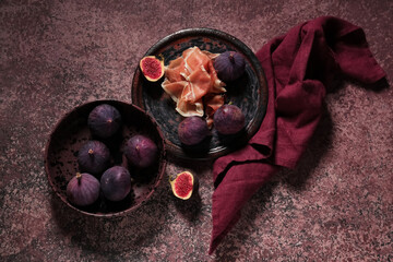 Plate with delicious prosciutto slices and fresh figs on purple background