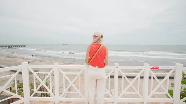 Rear view of a blonde woman enjoying the scenic ocean view from a white wooden pier, puerto colombia