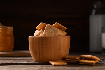Composition with bowl of tasty crackers on brown wooden table, closeup