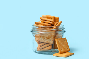 Glass jar with tasty crackers on blue background, closeup