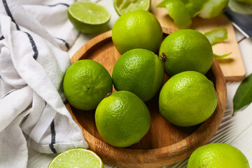 Plate with fresh ripe limes on white wooden background, closeup