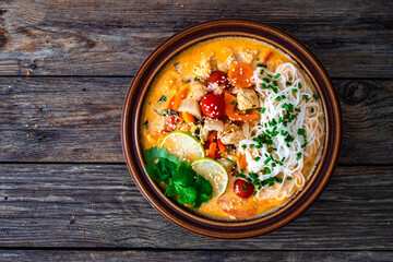Tom Yum soup - Thai soup with chicken breast nuggets, vegetables and rice noodles on wooden table. Top view
