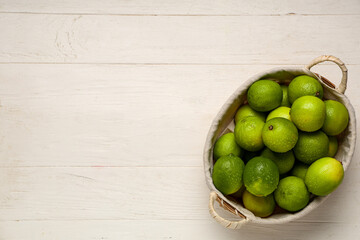 Wicker basket with fresh ripe limes on white wooden background