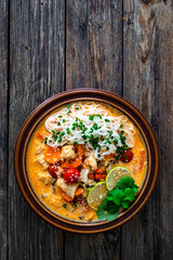 Tom Yum soup - Thai soup with chicken breast nuggets, vegetables and rice noodles on wooden table. Top view

