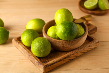 Bowl and cutting board with fresh ripe limes on wooden background, closeup