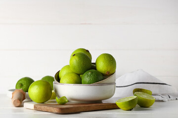 Bowl with fresh ripe limes on white wooden background