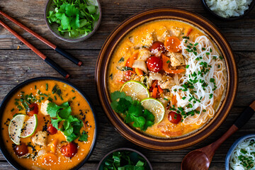 Tom Yum soup - Thai soup with chicken breast nuggets, vegetables and rice noodles on wooden table. Top view

