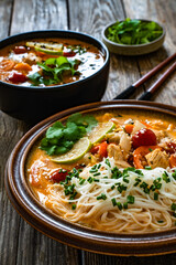 Tom Yum soup - Thai soup with chicken breast nuggets, vegetables and rice noodles on wooden table	
