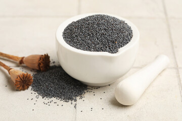 Mortar with poppy seeds and pestle on white tile background, closeup