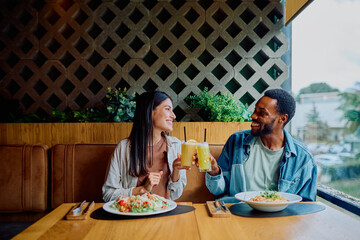 Happy multicultural couple enjoying a meal and toasting drinks at a modern restaurant, celebrating their time together