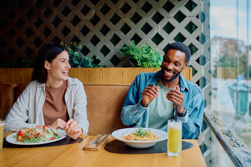 Diverse couple laughing and communicating during lunch at a restaurant, enjoying the relaxed and happy atmosphere