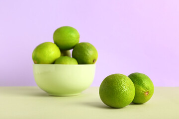 Bowl with fresh ripe limes on green table against lilac background
