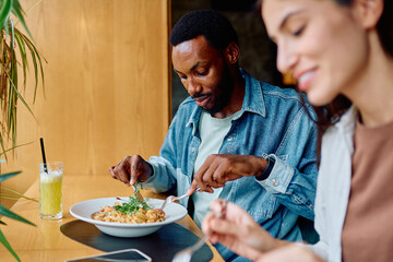 Black man and Caucasian woman enjoying lunch, eating pasta and drinking drinks at a modern restaurant