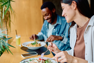 Diverse couple smiling, eating food and enjoying a pleasant lunch date at a modern restaurant. Sharing a happy lifestyle moment