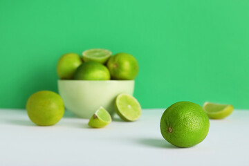 Bowl with fresh ripe limes on grey table against green background