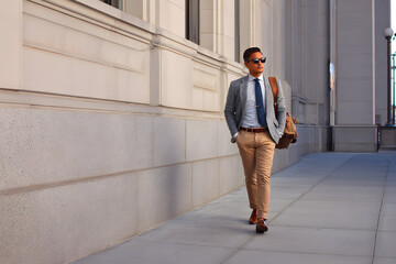 Urban Stroll of a Professional: A well-dressed individual strides confidently along the sidewalk beside a grand building, embodying urban sophistication and professional demeanor.