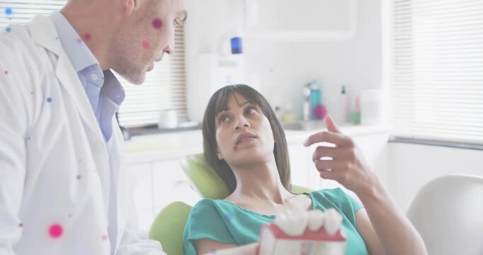 Dentist picking dental model explaining brushing while patient rotating model under colored overlay