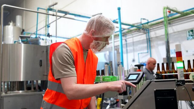 Brewery worker operating beer bottling labeling machine on conveyor belt