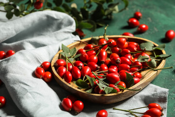 Wooden plate with fresh rose hip berries and leaves on green background, closeup