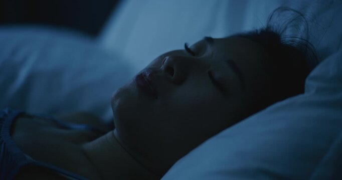 Portrait of Beautiful Asian Girl in Bed At Night, Restless and Uneasy. Woman Tosses and Turns in Sleep, Face Tense, Reflecting Unpleasant Dreams. Concept Insomnia, Bad Rest, Nightmares. Static Shot.