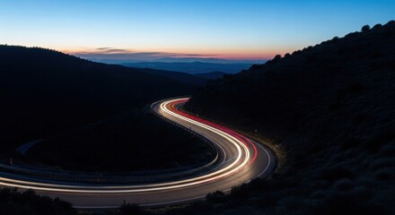 Curved mountain road at dusk with light trails and scenic horizon
