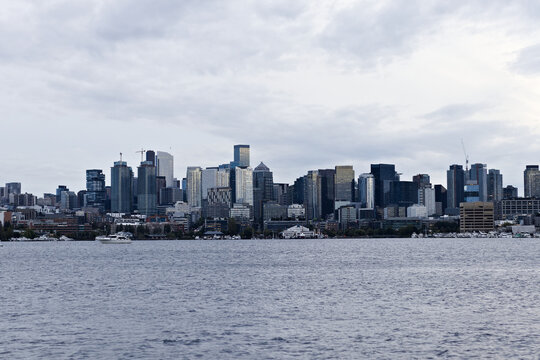 Downtown skyline view with tall buildings and boats on calm water under a cloudy sky, showcasing urban development and modern architecture.