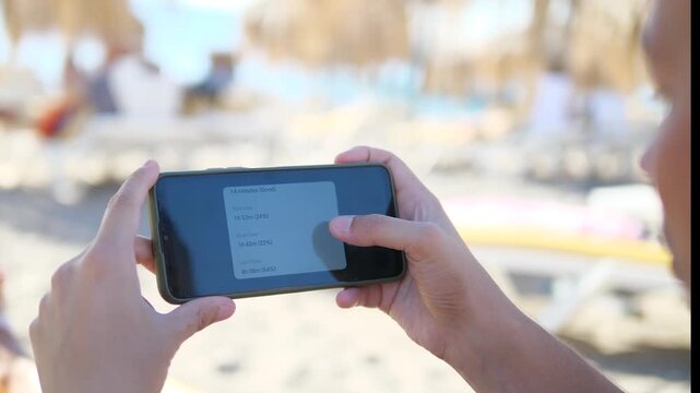 A mans hands on a sunny beach navigate a health application, scrolling through comprehensive metrics, statistics, and graphs related to his daily steps, physical activity, and sleep patterns. 