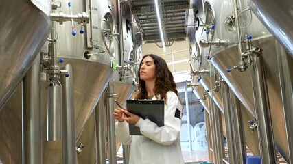Female brewmaster inspecting stainless steel tanks in a brewery - Powered by Adobe