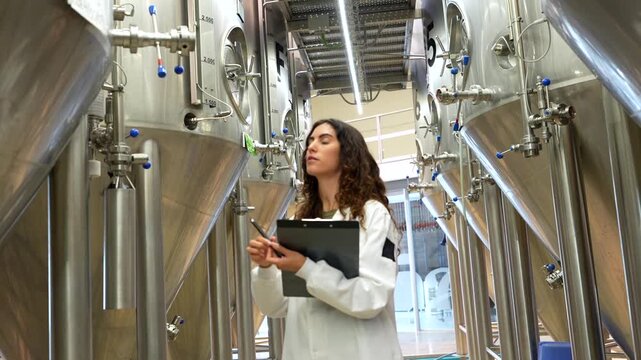 Female brewmaster inspecting stainless steel tanks in a brewery