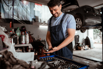 Mechanic working in garage smiles while checking tools on a busy workbench