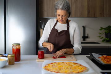 Senior woman preparing pizza in modern kitchen