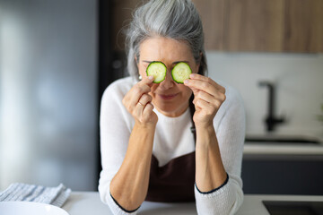 Senior woman holding cucumber slices over her eyes