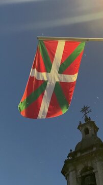 The Basque Country flag (Ikurri&ntilde;a) waving gracefully at night, illuminated by the soft glow of the moon. The scene captures the beauty and symbolism of the Basque identity, with gentle movement and dr