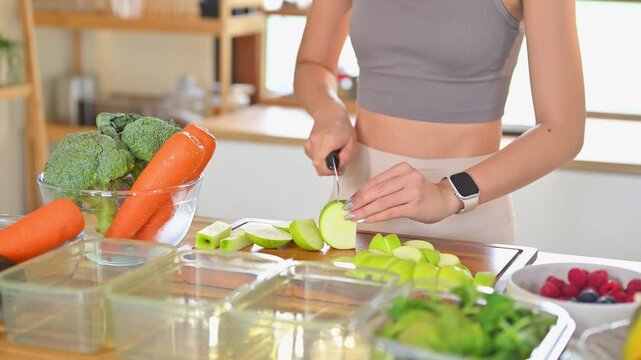 Young woman slicing green apples on a cutting board surrounded by fresh fruits and vegetables. Concept of weekly meal prep