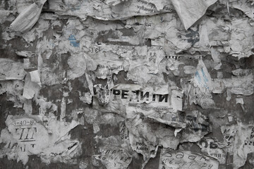 A dirty notice board filled with paper notices. Paper ads on a shabby wall. Rental, sale, help...