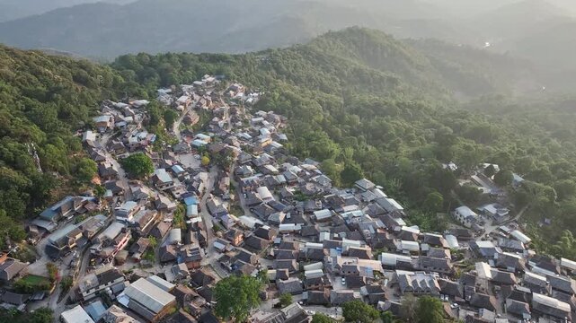 Aerial view of Mangjing Village nestled amidst lush green hills, the rooftops creating a patchwork quilt of textures and tones, Mangjing Village, Yunnan, China.