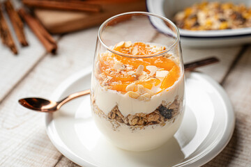 Healthy yogurt dessert served in a glass with granola, dried fruits and apricot jam, topped with almond flakes