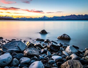 Rocky shore, calm lake, snowy mountains at sunset hues