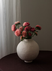 Bouquet of asters in a ceramic vase on a round table with a brown tablecloth