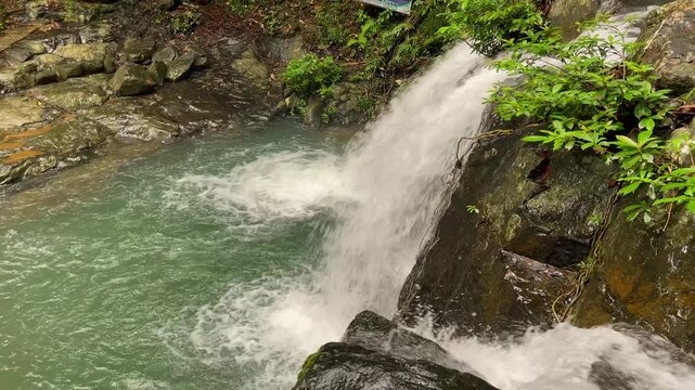 Overhead high angle view of Salakot Falls pouring over dark wet rock into a turquoise pool with foam patterns and dense tropical forest plants
