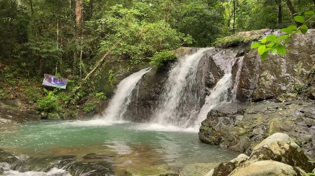 Wide waterline view of Salakot Falls with three white cascades dropping over dark rock into a shallow turquoise pool in dense tropical forest