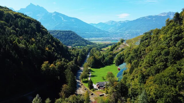 Aerial view of Mines de Sel de Bex nestled in a valley with lush green trees contrasting against the bright blue sky and distant mountains, Bex, Vaud, Switzerland.