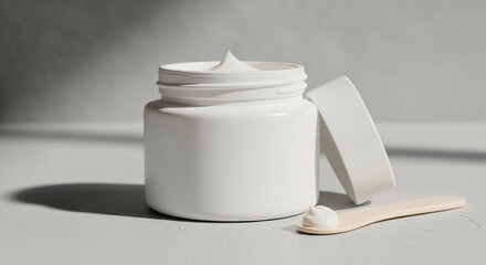 Closeup shot of a white cosmetic cream jar with a wooden spatula on a neutral surface, showcasing skincare product and its packaging in a minimalist setting