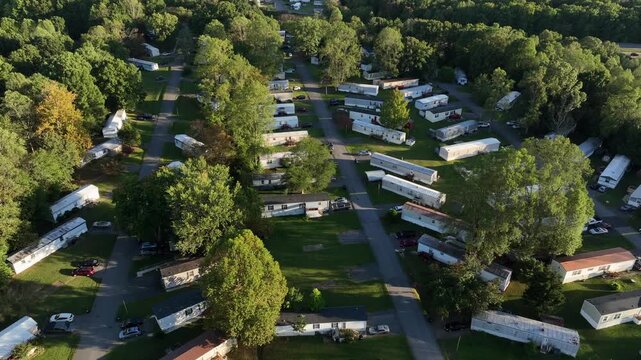 Aerial view of america trailer park community in United States. Rows of mobile homes surrounded by green trees on sunny afternoon, showing suburban life in rural America. Top down.