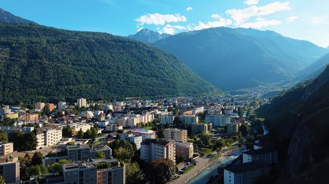 Aerial view of Martigny nestled between verdant mountain slopes and a clear river, creating a striking contrast of urban and natural elements, Martigny, Valais, Switzerland.