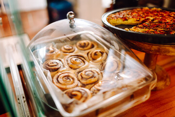 A transparent display case full of various sweets in cozy coffee shop. Freshly baked cinnamon rolls and delicious pie in bakery. A cozy atmosphere. Concept is consumerism, small business, and food.