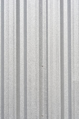 Fototapeta premium A vertical close-up of a gray corrugated metal fence or sheeting with a sparkling, granular texture and visible vertical ribs