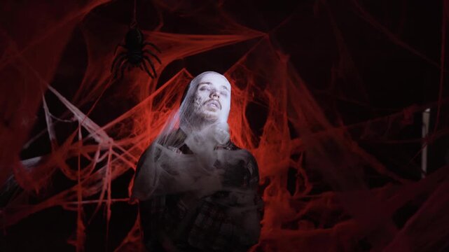 Dramatic zombie man trapped in spiderwebs sleeping on red background. Halloween fantasy horror scene.