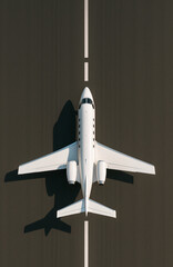 An overhead view of a luxury private jet on the runway, shot in minimalist daylight. The sleek and modern business jet symbolizes wealth, success, and an exclusive lifestyle.